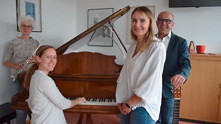Vier Personen stehen um ein Klavier herum und lächeln in die Kamera.